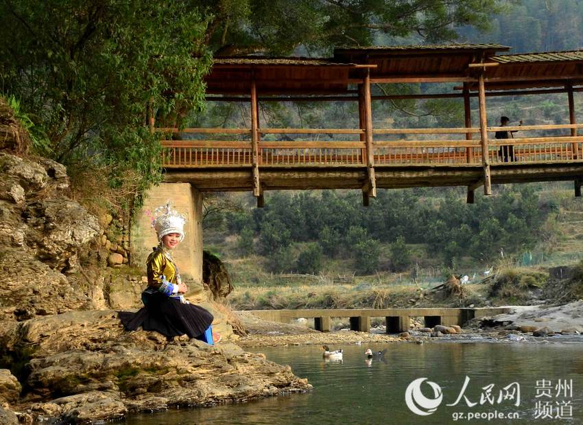 2016年2月11日，在贵州省从江县，乡村春意渐浓，景色迷人，一位壮族姑娘在村边的小河旁游玩。