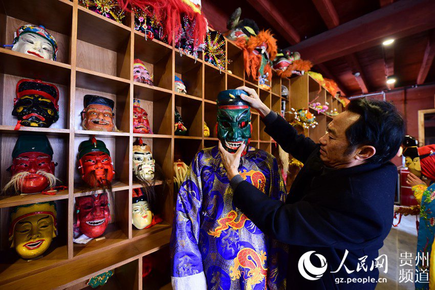 1月16日，福泉阳戏传承人周昌智（右）在为村民佩戴面具。