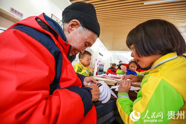 10月22日，小朋友在貴州省畢節市七星關區柏楊林街道易地扶貧搬遷安置點的日間照料中心內與老人一起剪紙。陳曦 攝