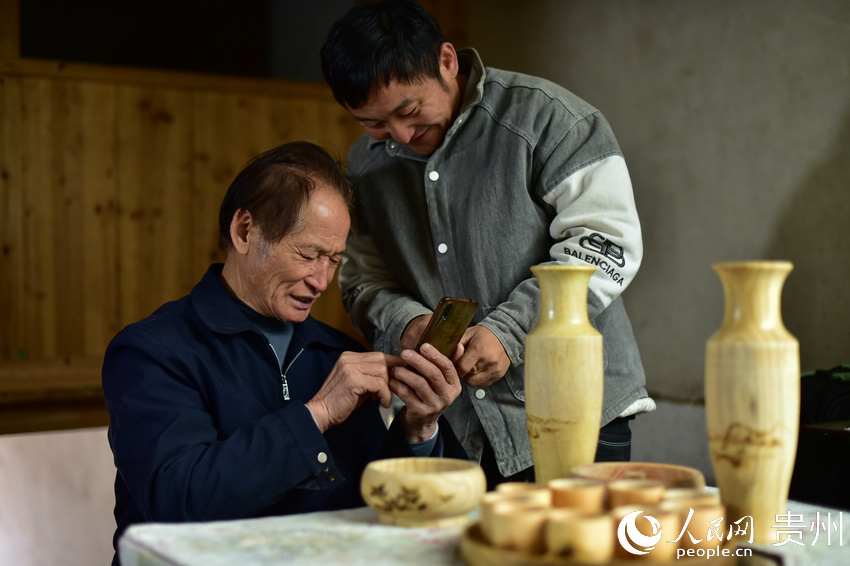 貴州省丹寨縣龍泉鎮一木藝加工作坊，吳明章（左）在好友的指導下學習使用智能手機。