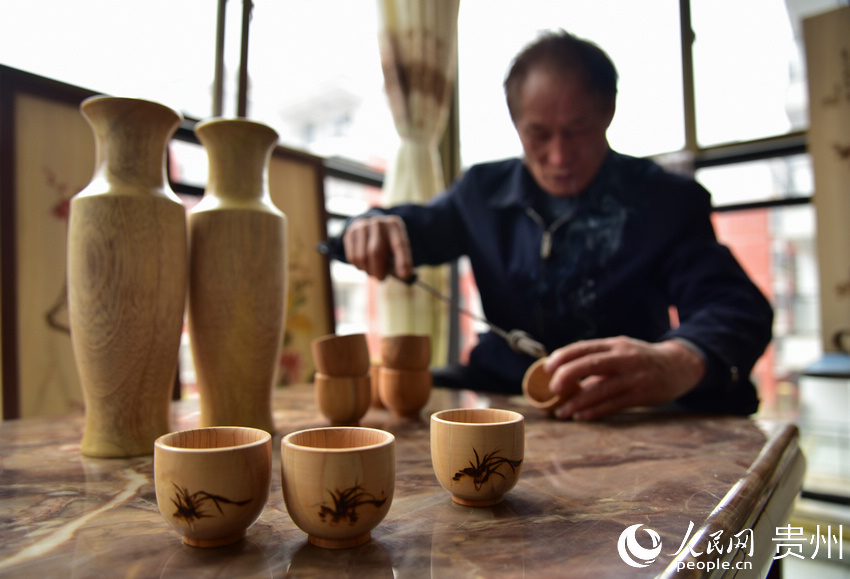貴州省丹寨縣金泉街道易地扶貧搬遷安置區，吳明章在為好友制作的木質茶杯進行免費的烙畫創作。