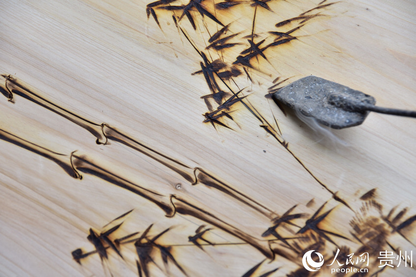 貴州省丹寨縣金泉街道易地扶貧搬遷安置區，吳明章在一塊經過處理的廢舊木板上進行烙畫創作。