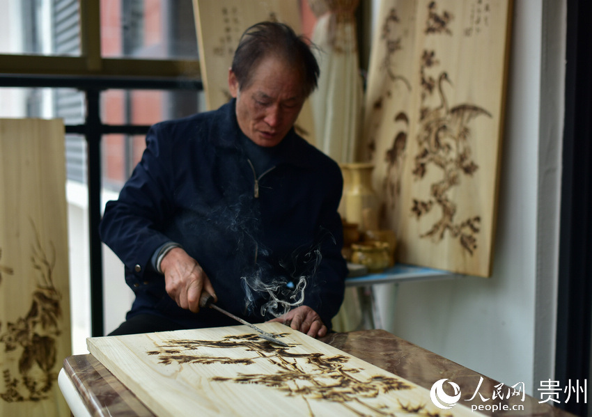 貴州省丹寨縣金泉街道易地扶貧搬遷安置區，吳明章在一塊經過處理的廢舊木板上進行烙畫創作。