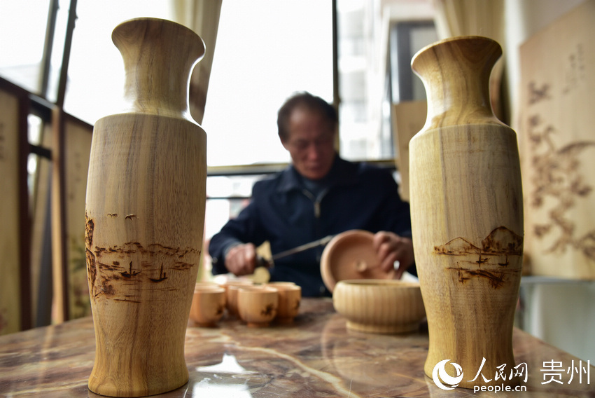 貴州省丹寨縣金泉街道易地扶貧搬遷安置區，吳明章在為好友制作的木質器具進行免費的烙畫創作。