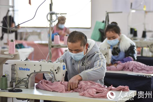 1月14日，在贵州省丹寨县金钟经济开发区，龙明贵(前)在服装加工车间加工服装。