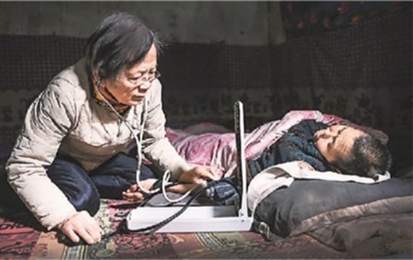 2021年1月18日，在陕西省榆林市佳县店镇贺家沟村农家窑洞里，路生梅跪坐在土坑上为瘫痪不起的村民义诊。新华社记者 陶 明摄