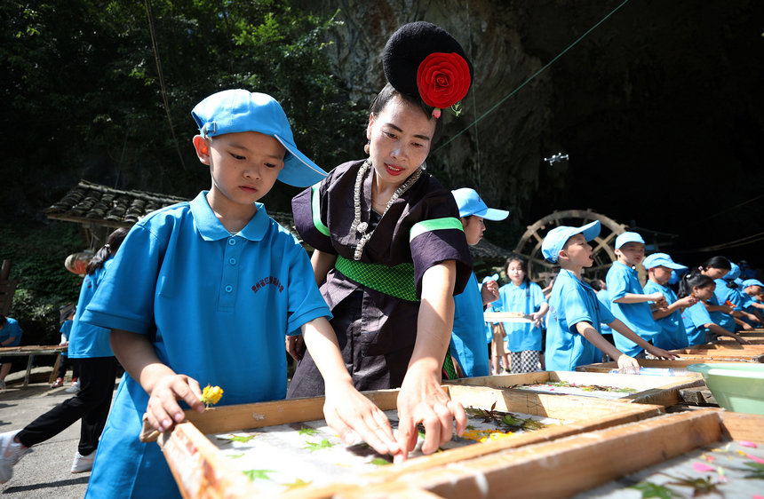 7月25日，造纸工匠在造纸作坊指导小学生制作花草纸。