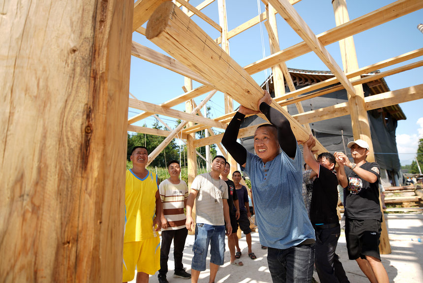8月4日,村民们在校正吊脚楼房架的“排柱”。