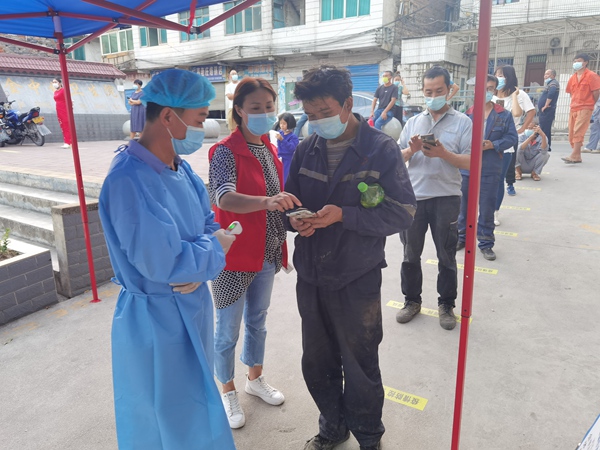 图为：社区志愿者冉蕊、唐晋在卫生院核酸采集点协助开展全民核酸检测工作