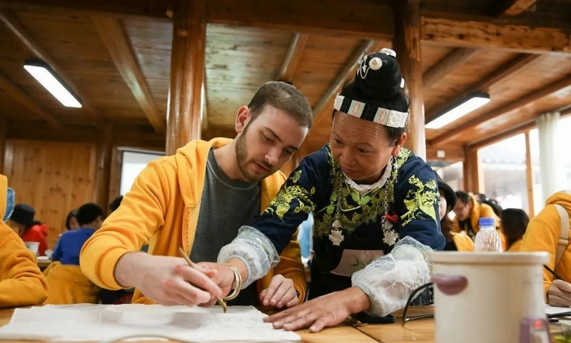 苗族蜡染艺人在教游客使用传统蜡刀绘制蜡画。