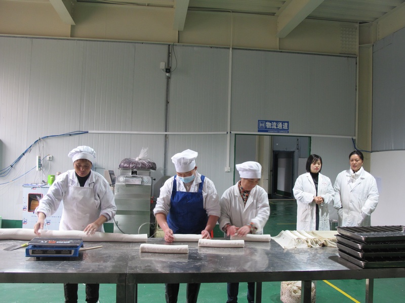思南百味福公司董事长周仕平（右二）向客人介绍花甜粑生产情况。陈时安摄