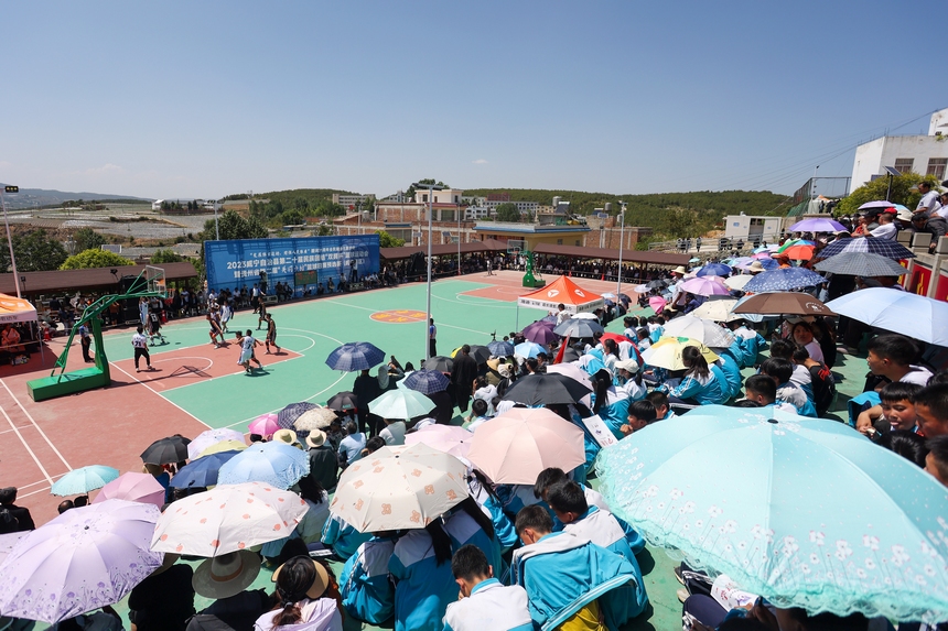 5月23日，在貴州省威寧縣牛棚鎮觀看當地舉辦的民族團結“雙擁杯”籃球賽比賽現場，群眾打傘在烈日下觀看比賽。