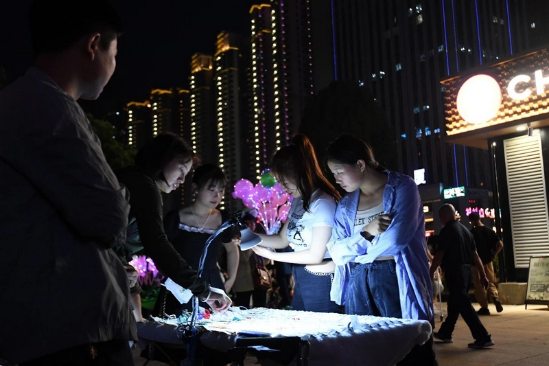 市民游客在南明区花果园湿地公园广场夜市摊位购买饰品。