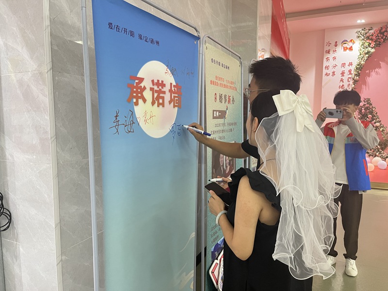 图为：承办七夕节“我们的节日·七夕心港湾”活动中，一对新人在婚事新办承诺墙上签名