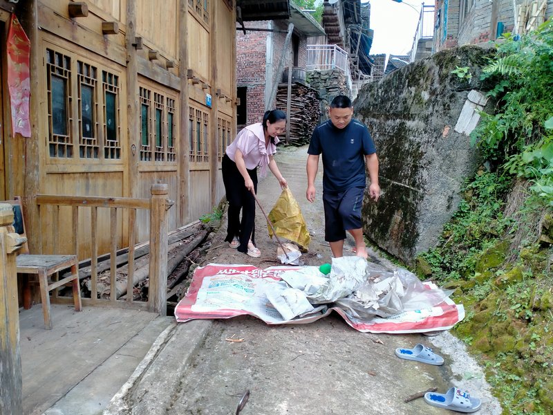 石登蘭（左一）與駐村干部楊愛民幫助外出務工戶清理柴草。