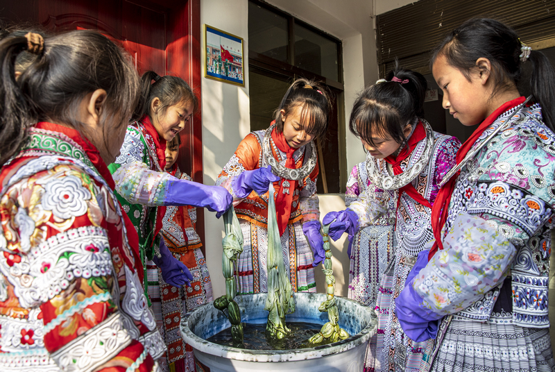 2023年12月28日，贵州省黔西市林泉镇高锦社区高锦小学，学生在染缸里对完成捆扎的白色布料进行反复扎染。