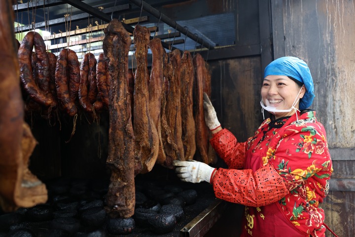 蔗香镇蔗香村妇女整理烤架上的腊肉。