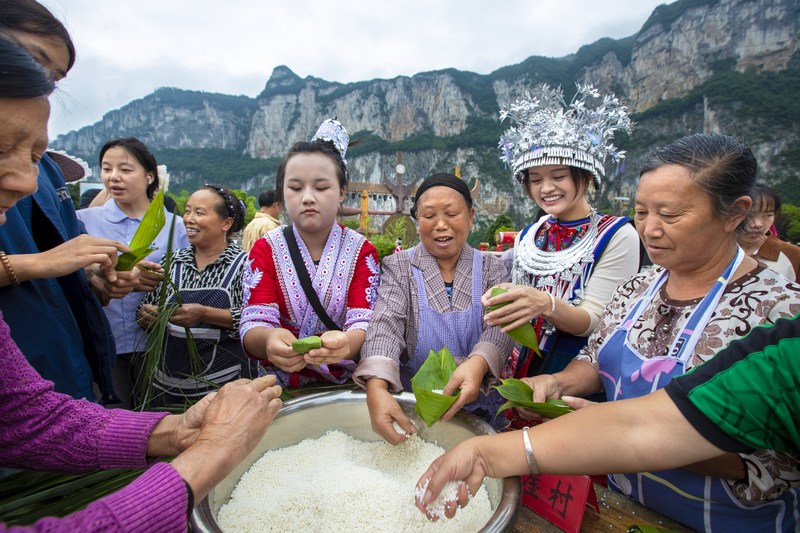 6月7日，貴州省畢節市黔西市新仁苗族鄉化屋村，村民們和游客包粽子。