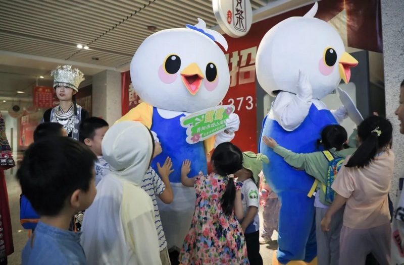 工作人员、卡通人偶“鹭鹭”、苗族姑娘在贵阳东站迎接萌娃团。