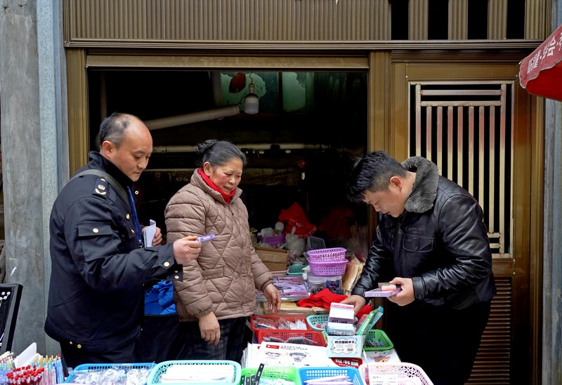 2025年2月17日，贵州省毕节市纳雍县第一小学旁，检查组在查看校园周边摊点售卖物品。杨英摄