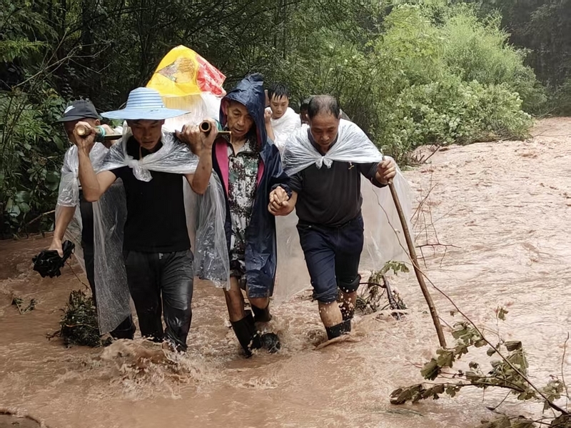 暴雨中村民抬伤者蹚过浑浊积水路。习水县融媒体中心供图