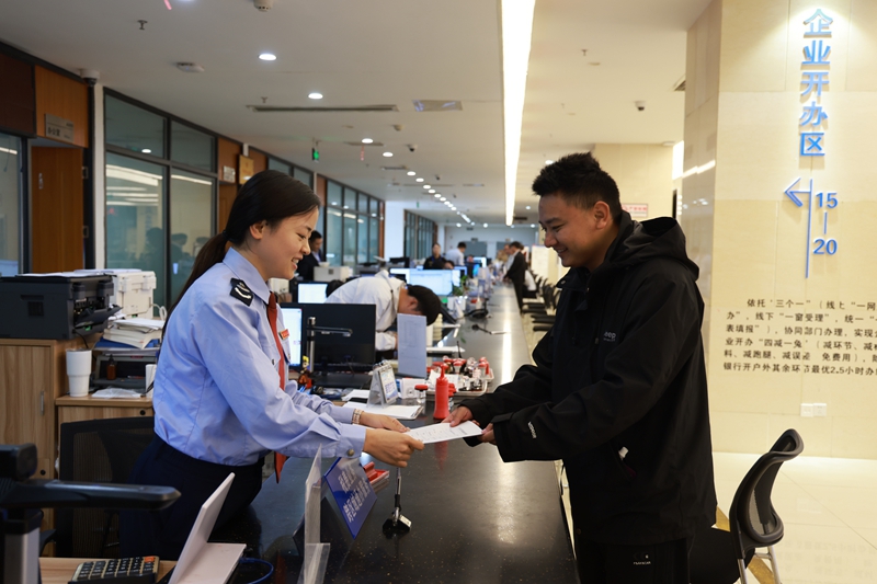 图为税务干部为纳税人办结税务事项并讲解相关税费优惠政策。漆毓摄