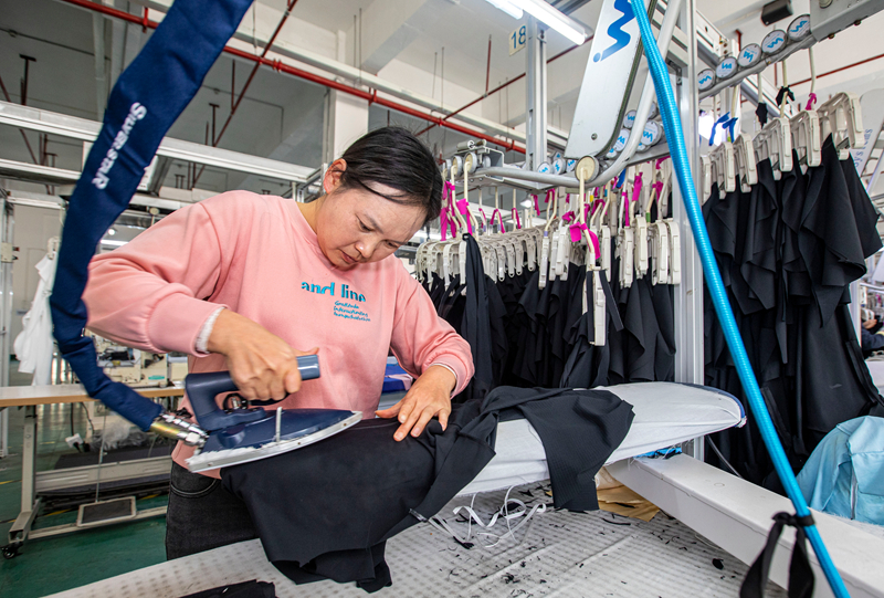 工人在贵州省毕节市黔西市经济开发区一家服饰企业车间生产线上熨烫服饰。