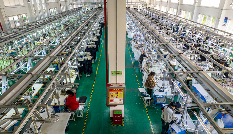 工人在贵州省毕节市黔西市经济开发区一家服饰企业车间生产线上加工服饰。