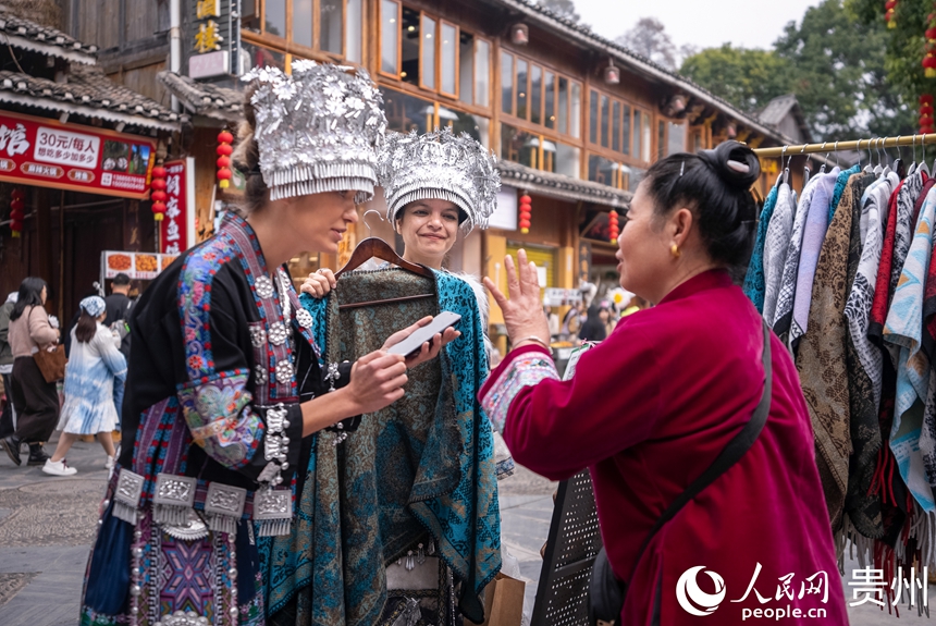 12月20日,来自国外的游客身着当地少数民族同胞盛装选购商品。人民网记者 涂敏摄