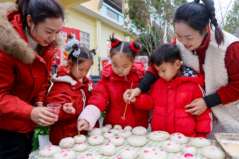 2025年12月31日，贵州省黔东南苗族侗族自治州施秉县第五幼儿园的孩子们在老师的指导下给糍粑盖红印。（磨桂宾 摄）