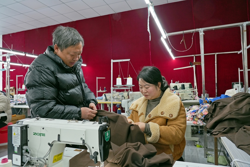 2026年1月12日，贵州省毕节市纳雍县化作乡银鑫制衣厂，负责人邓林海（左）在和员工讨论服装缝制针法。 