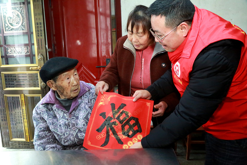 書法志願者在貴州省遵義市播州區龍坑街道八裡社區為102歲淳祖開老人送上書寫的“福”。