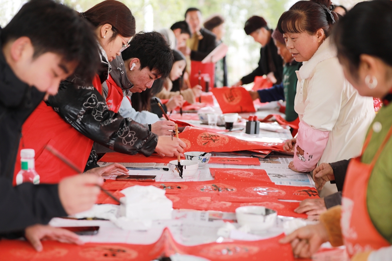 贵州省黔西市林泉镇营脚村村民在参加新春大联欢活动，大学生志愿者在给村民写春联。