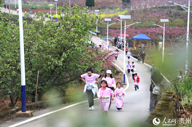参赛选手与市民游客奔跑在桃花掩映的乡村赛道。人民网 龙章榆 摄