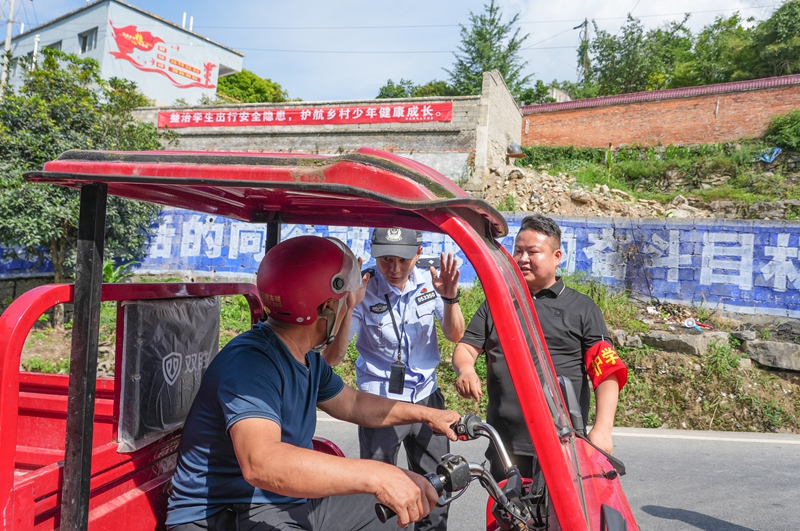 2026年6月4日，贵州省毕节市纳雍县乐治镇街路口，护学人员提醒家长不能非法搭载学生。  杨英 摄.jpg