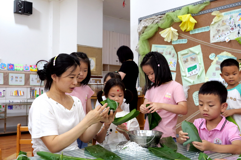 端午节前夕,在松桃实验幼儿园,老师一步步演示包粽子的步骤,孩子们认真观看后动手尝试。