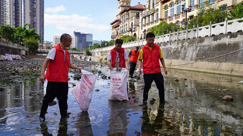 志愿者手持工具清理岸边垃圾、枯枝及河道漂浮杂物。