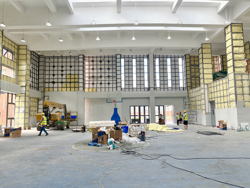 仁懷市蒼龍小學風雨操場提升改造項目施工現場，施工人員校准牆面、鋪貼吸音板材，全力優化場館聲學環境。