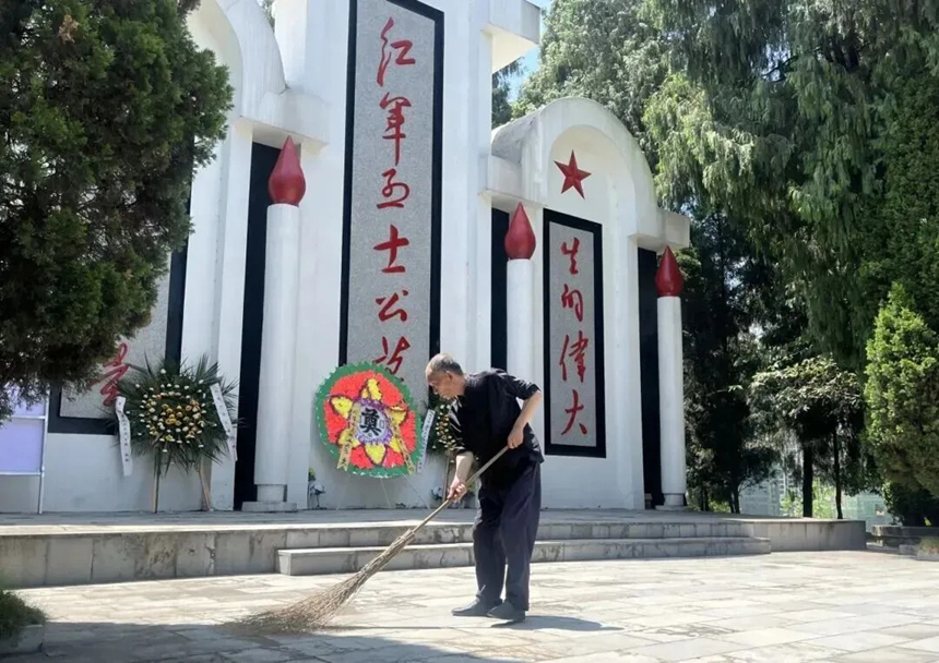郭德剛手持掃帚清掃魯班紅軍烈士陵園。